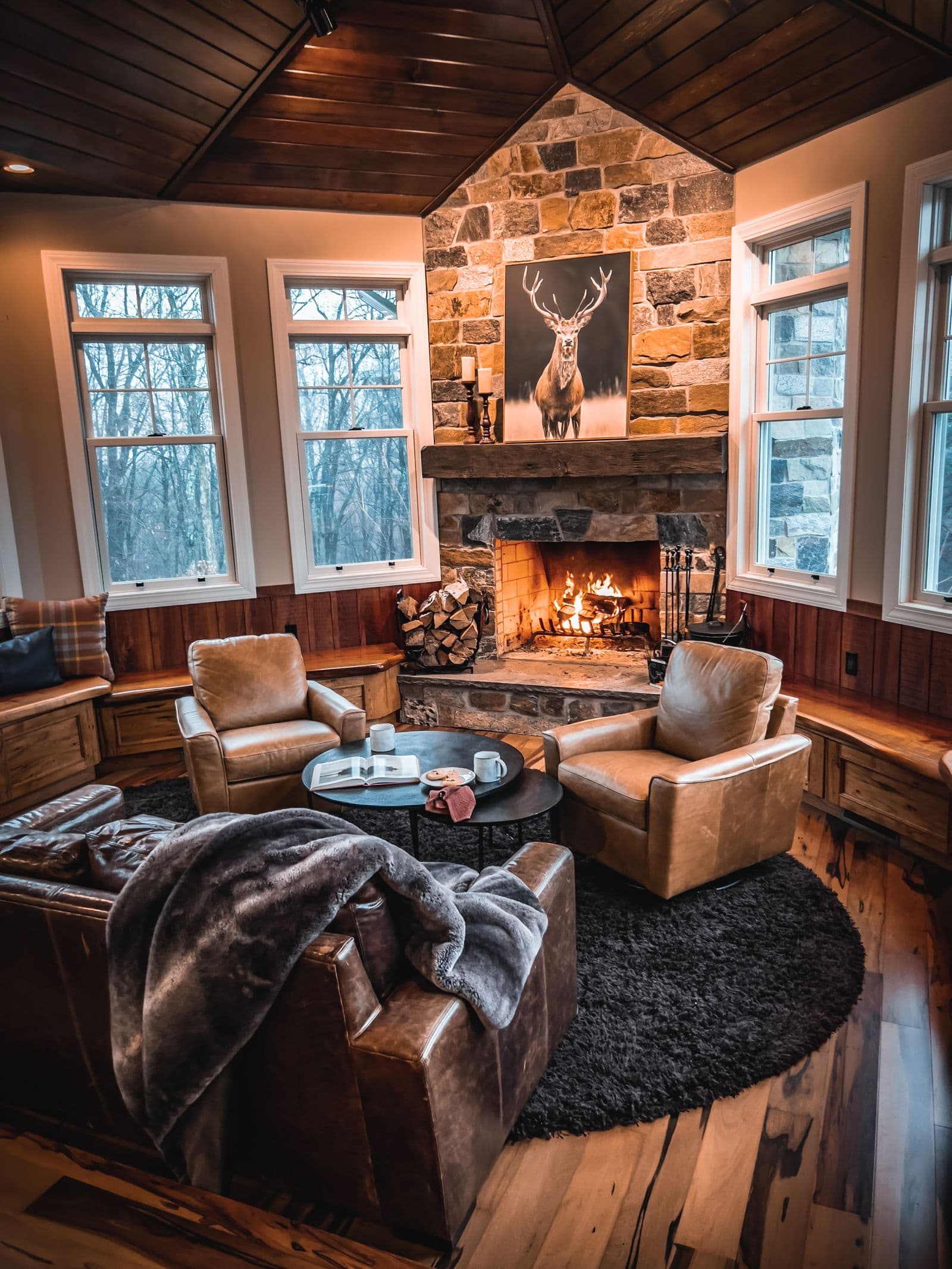 A warm cabin living room with a lit stone fireplace and leather armchairs